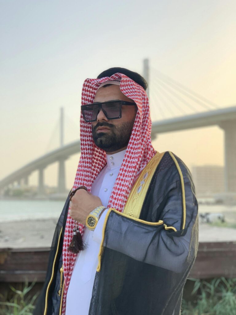 A fashionable man in a keffiyeh by a bridge, showcasing traditional Middle Eastern attire.